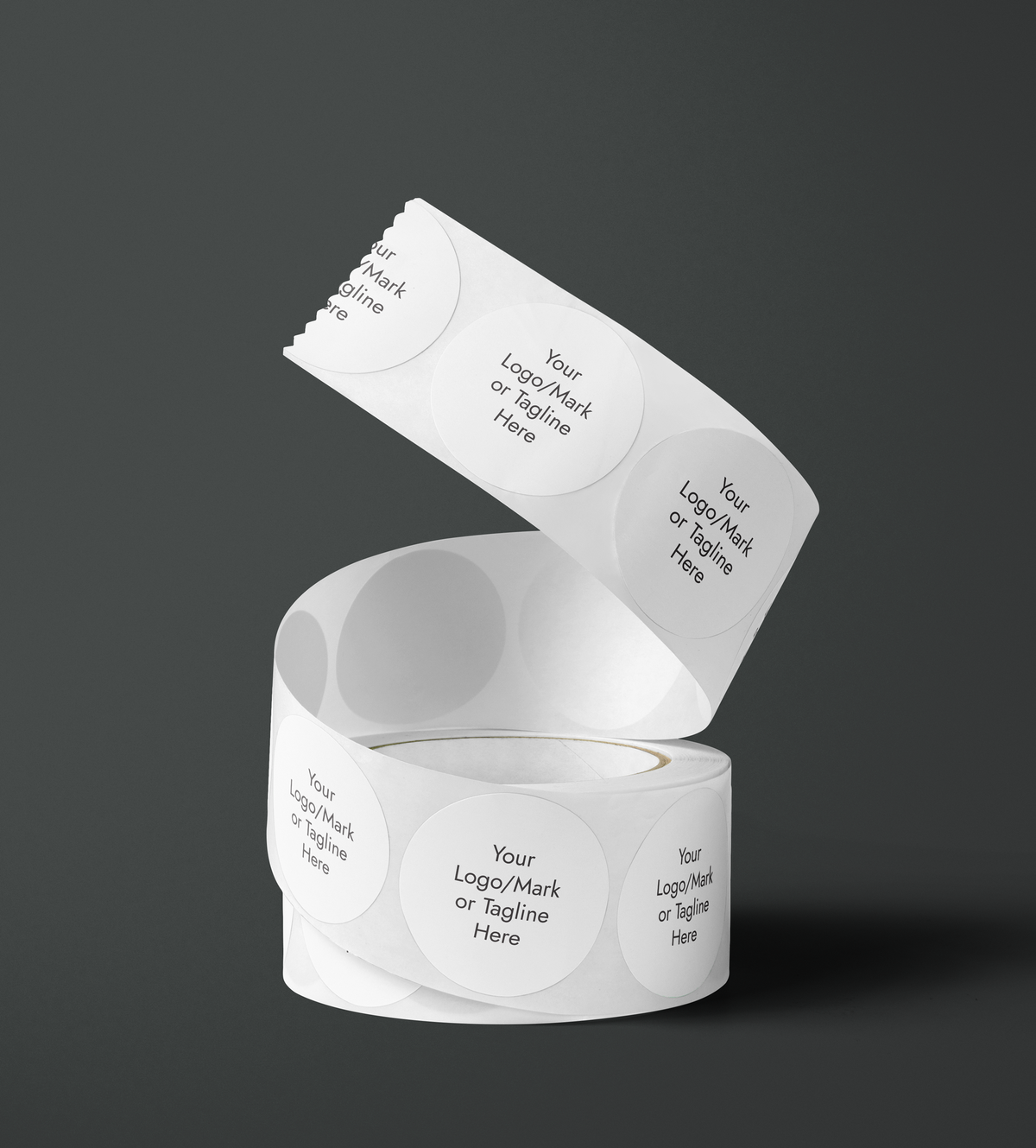 A roll of white paper labels or tape with repeated circular branding printed in black and white shown on a dark gray studio background. The visible text includes 'Your Logo/Mark or Tagline Here'. Fine Stationery & Paper Goods. Custom branded stickers.